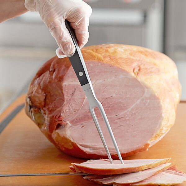 A person holding a Wusthof Classic carving fork over a piece of ham.
