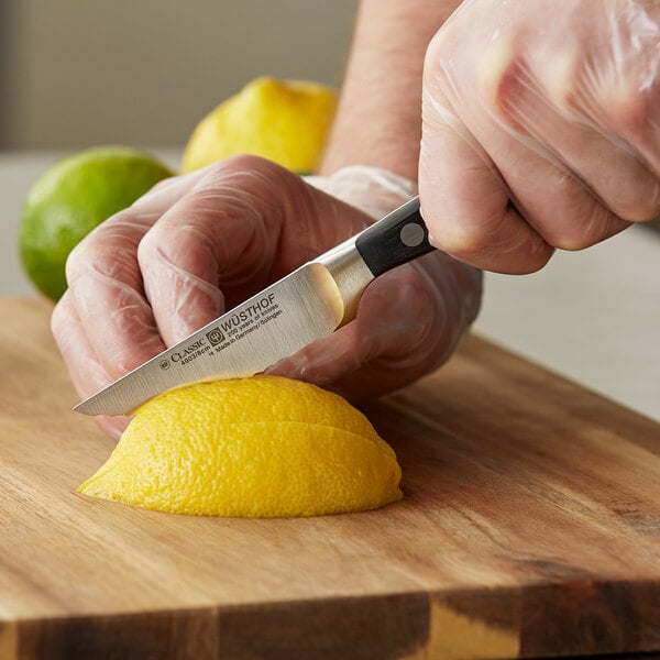 A person's hands using a Wusthof Classic serrated paring knife to slice a lemon.