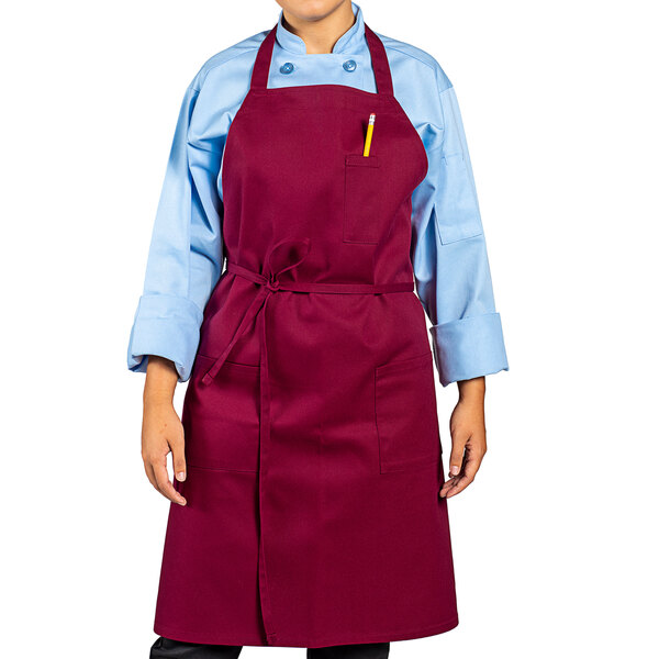 A woman wearing a red Uncommon Chef bib apron with three pockets.