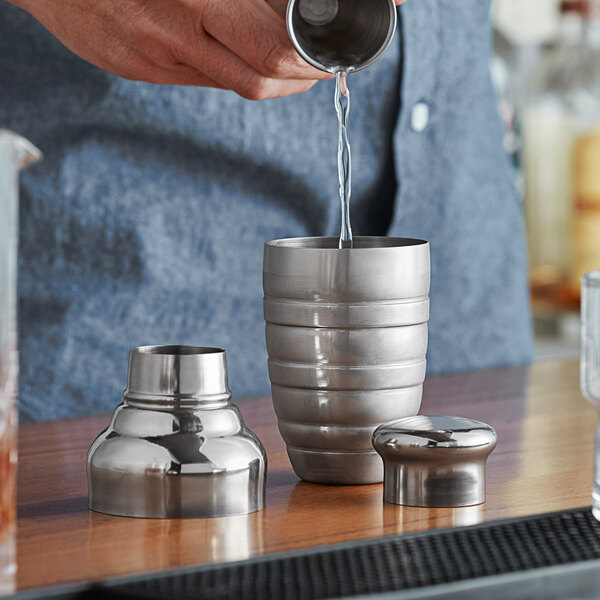 A man pouring liquid into an American Metalcraft stainless steel beehive shaker on a bar counter.