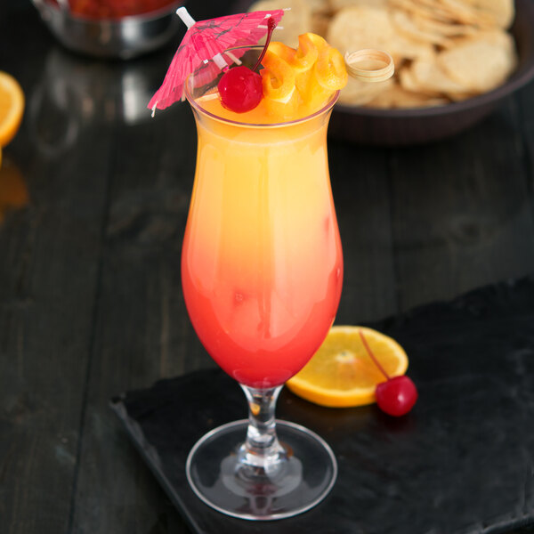 A Carlisle plastic hurricane glass with a drink, straw, and fruit garnish.