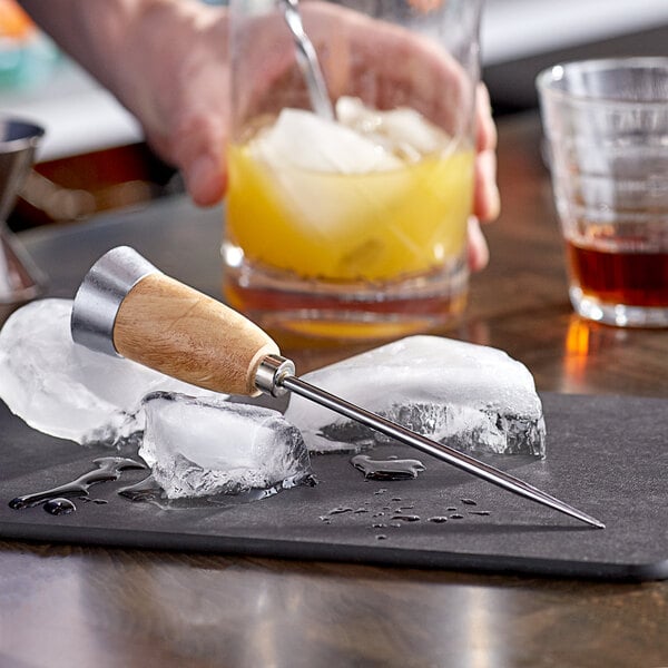 A hand using American Metalcraft steel ice pick with wooden handle to block ice for a drink.
