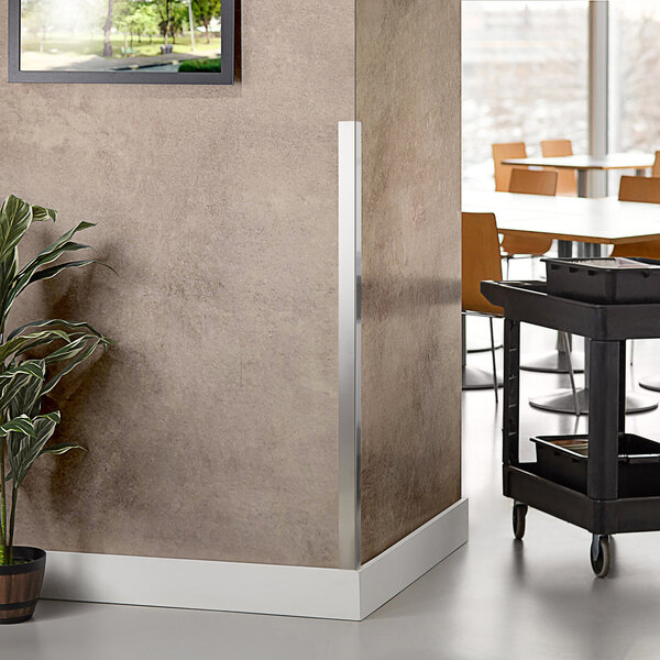 A stainless steel Regency wall corner guard on a wall next to a table with a tray and a plant.