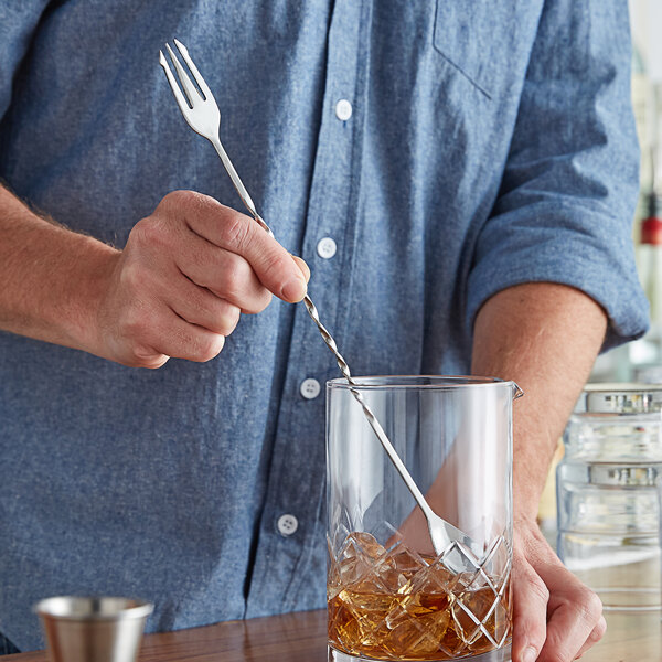 A person holding an American Metalcraft trident fork and stirring a drink in a glass.