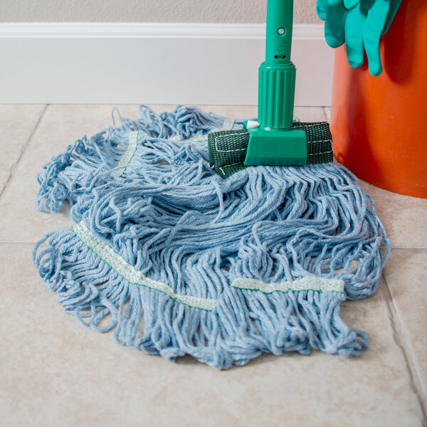A blue Carlisle Flo-Pac wet mop with a green headband on the floor next to a green mop bucket.