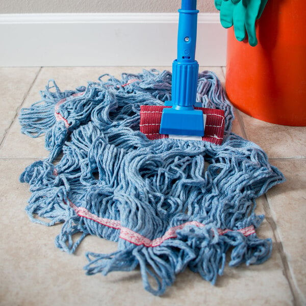A Carlisle blue cotton blend wet mop head with a red headband on the floor next to a red bucket.