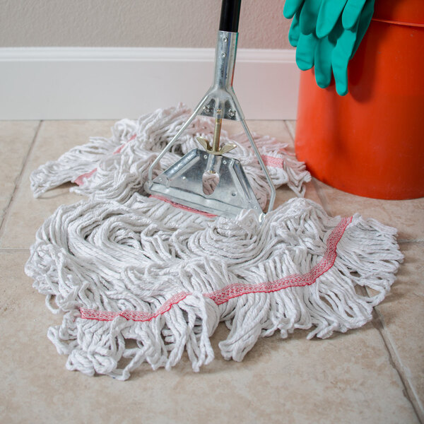 A Carlisle natural cotton wet mop with a red headband next to a bucket on the floor.