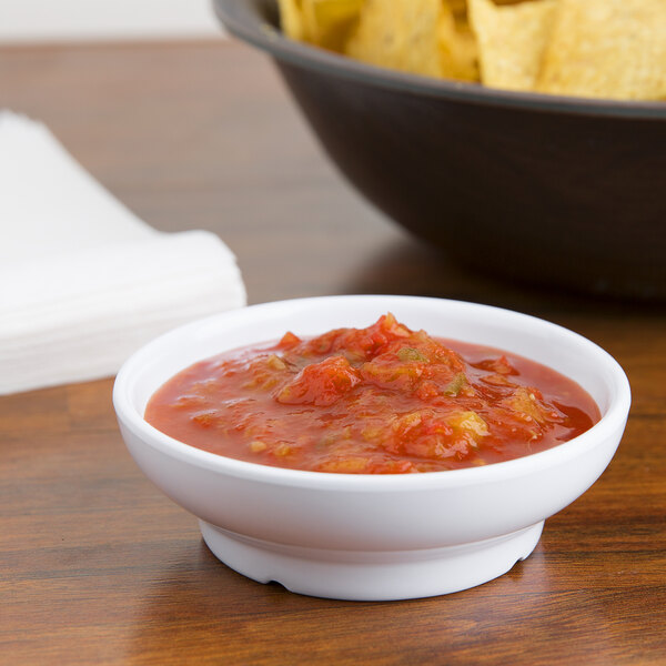 A white GET salsa dish filled with salsa next to a bowl of chips on a table.