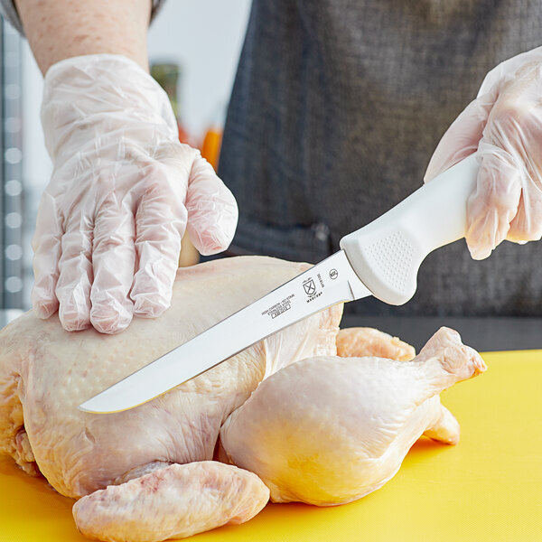 A person in gloves using a Mercer Culinary Ultimate White Boning Knife to cut a chicken.