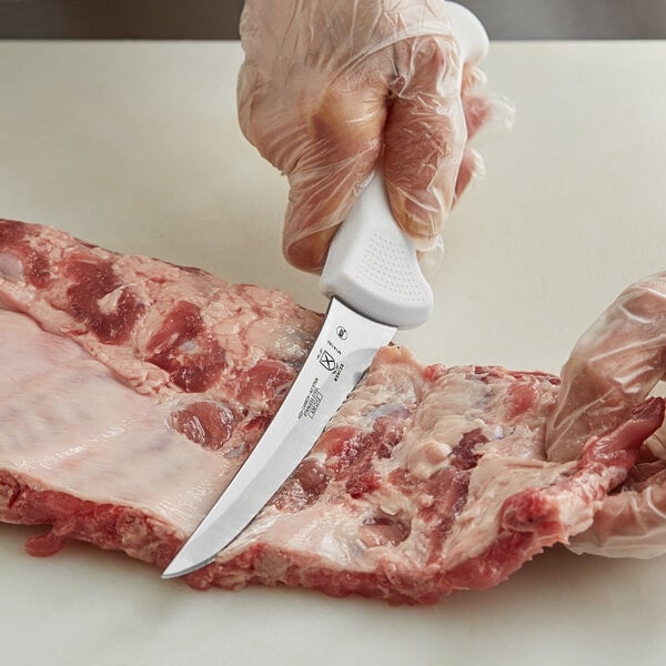 A person using a Mercer Culinary Ultimate White® curved boning knife to cut meat.