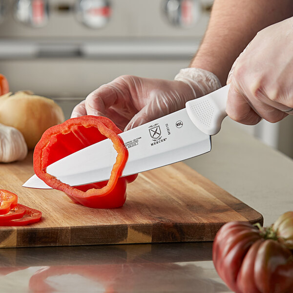 A person using a Mercer Culinary Ultimate White® Chef Knife to cut a red bell pepper.