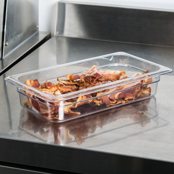 A clear plastic food pan with bacon in it.