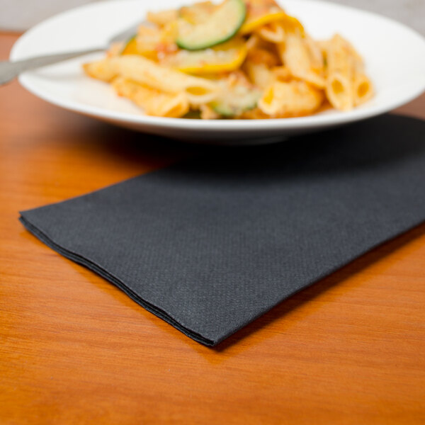 A plate of pasta and a fork on a Hoffmaster black dinner napkin.