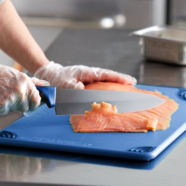 A person cutting meat on a blue cutting board with a Dexter-Russell 36005C 8" Chef Knife with a blue handle.