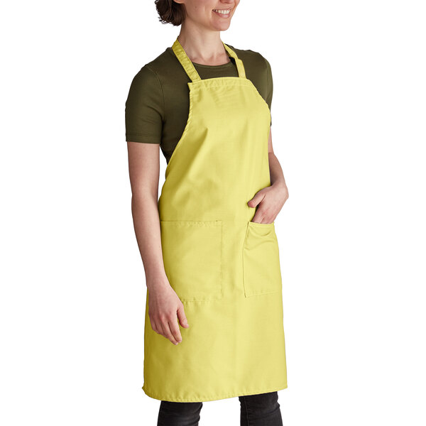 A woman wearing a yellow Intedge bib apron with 2 pockets.