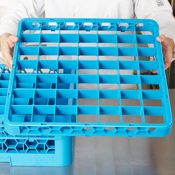 A person holding a blue Carlisle OptiClean glass rack extender with 49 compartments.