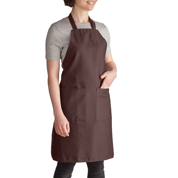 A woman wearing a brown Intedge bib apron with pockets.
