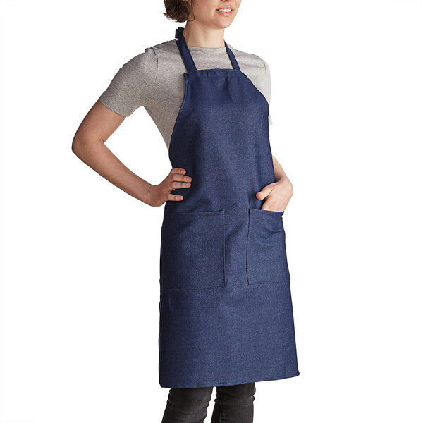 A woman wearing a denim Intedge bib apron with pockets in a professional kitchen.