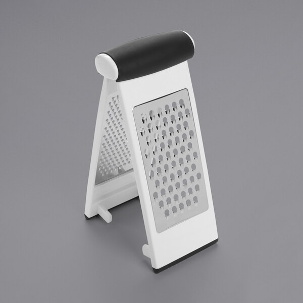 An OXO white plastic and stainless steel cheese grater on a gray surface.