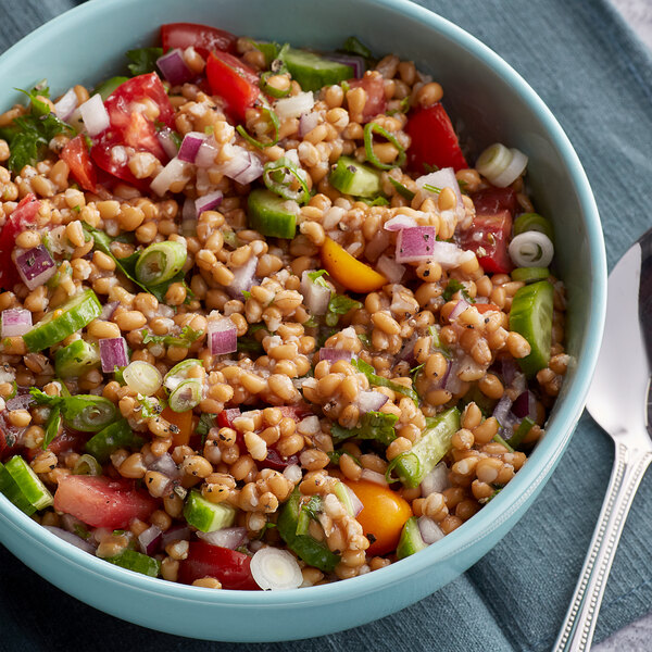 A bowl of Farro salad with tomatoes, onions, and cucumbers on a table.