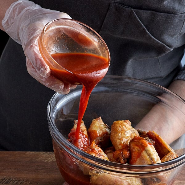 A person pouring TABASCO® Scorpion Hot Sauce onto a bowl of chicken wings.