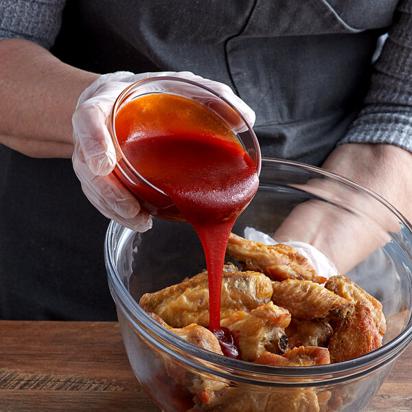 A person pouring TABASCO Sweet & Spicy Hot Sauce into a bowl of chicken wings.