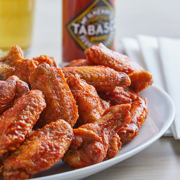 A plate of fried chicken wings with a bottle of TABASCO® Scorpion Hot Sauce on a table.