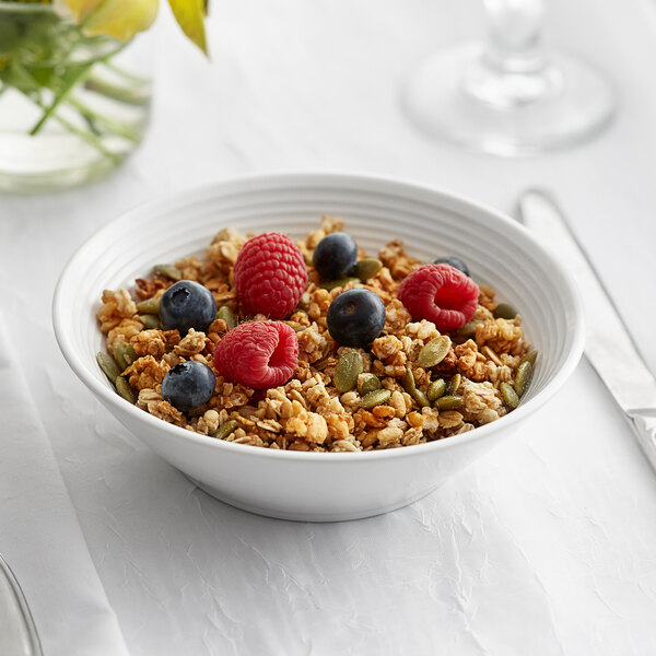 A bowl of cereal with berries and nuts in a bright white bowl with embossed lines on the rim.