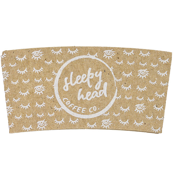 A brown cardboard coffee cup sleeve with white text that says "Sleepy Head" and has eyes and a circle.