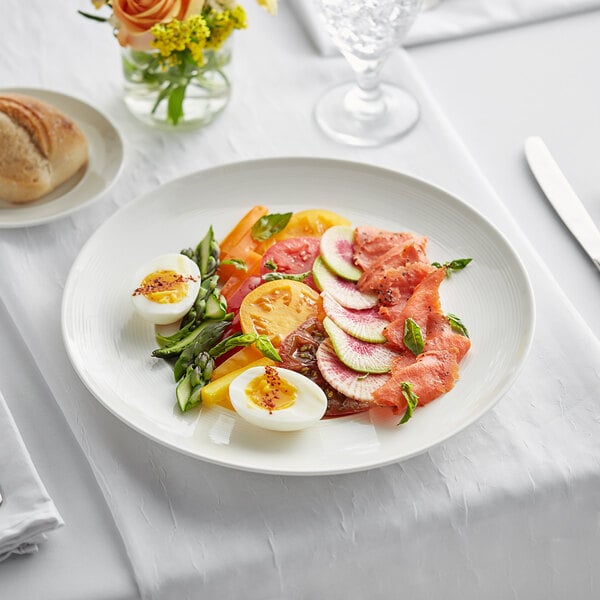 An Acopa Liana porcelain plate with a salad, eggs, and vegetables on a table.