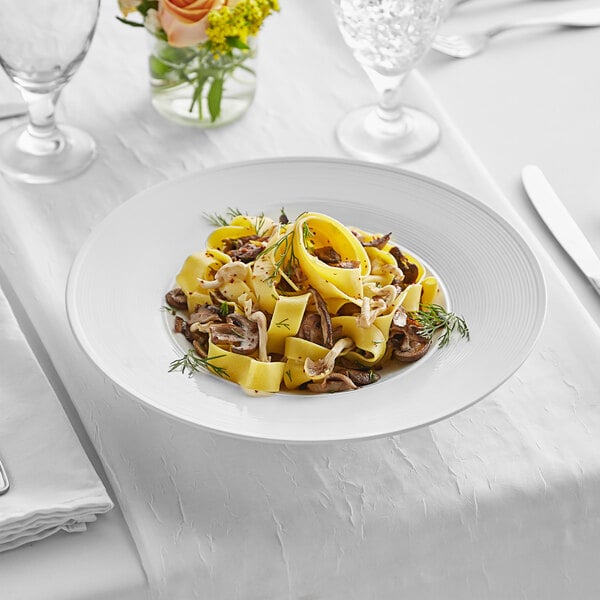 A white Acopa Liana porcelain pasta bowl filled with pasta and mushrooms on a table.
