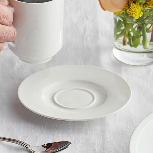 A hand holding a white mug over a white Acopa Liana saucer.