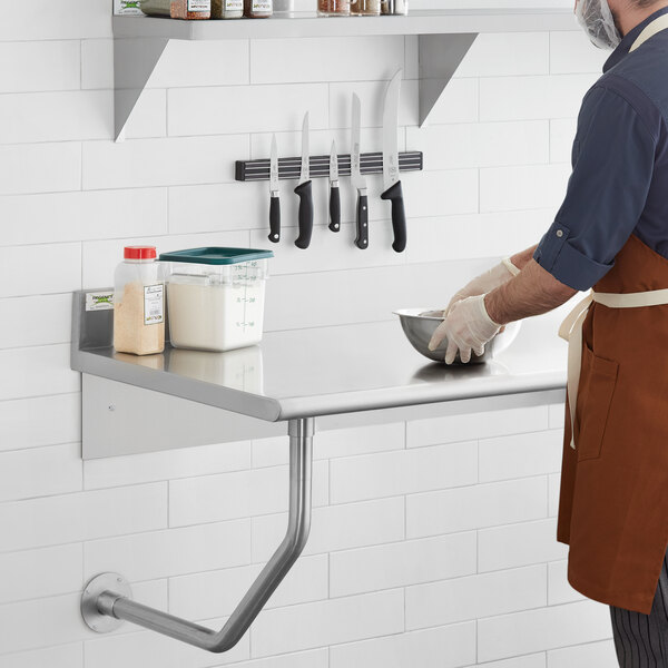 A man in a brown apron using a Regency stainless steel wall mounted table in a professional kitchen.