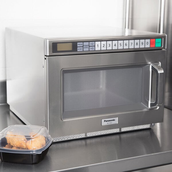 A Panasonic stainless steel commercial microwave oven with a container of food on top.
