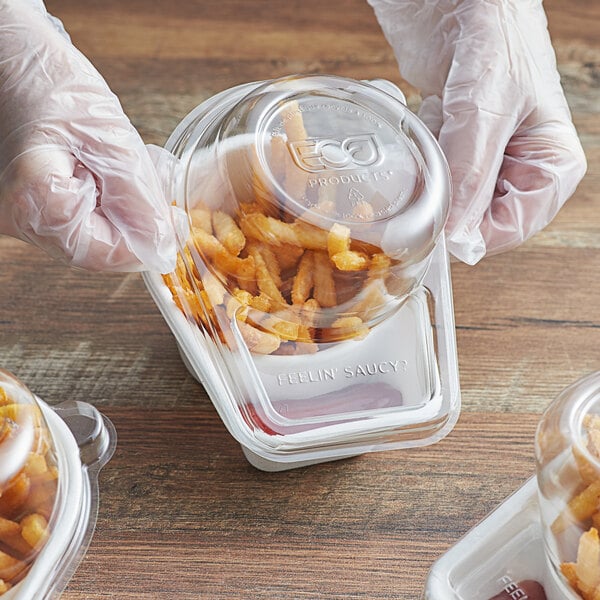 A person in gloves using a Eco-Products 2-compartment plastic container with a plastic lid to put french fries in.