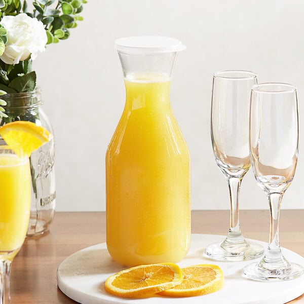 A Choice polycarbonate carafe filled with orange juice on a table with glasses.