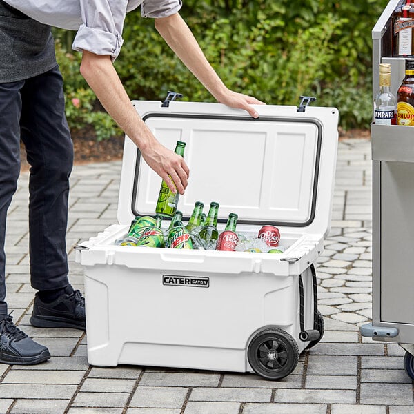 A man putting bottles of beer into a white CaterGator outdoor cooler with ice.