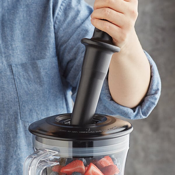 A person using a black AvaMix tamper in a blender with strawberries.