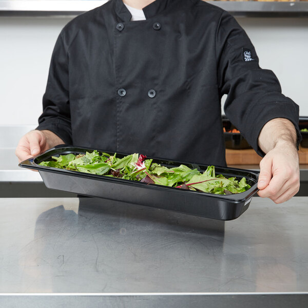 A chef holding a Cambro black polycarbonate food pan filled with salad.
