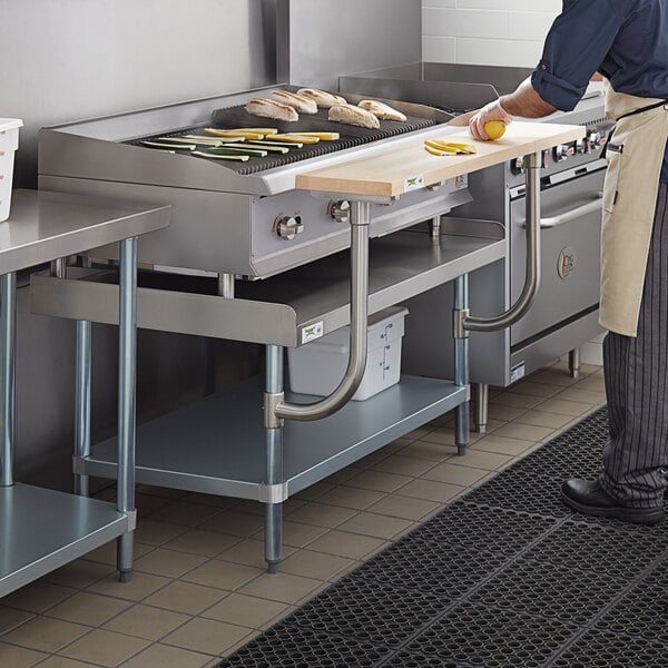 A man using a Regency stainless steel equipment stand with a wooden cutting board in a commercial kitchen.