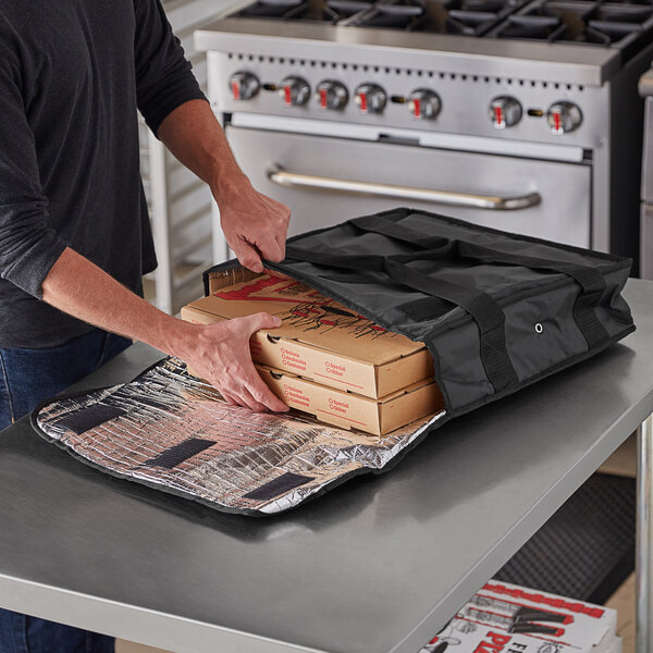 A man putting pizza boxes in an American Metalcraft deluxe black polyester pizza delivery bag.