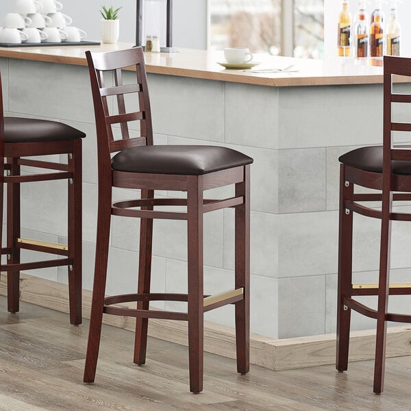 Three Lancaster Table & Seating mahogany wood bar stools with dark brown vinyl seats on a bar counter.