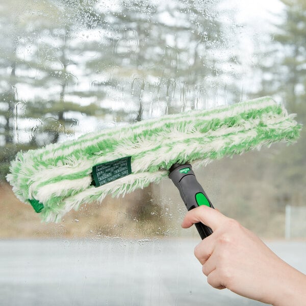 A hand using a Unger Monsoon Plus StripWasher with a green and white mop to clean a window.