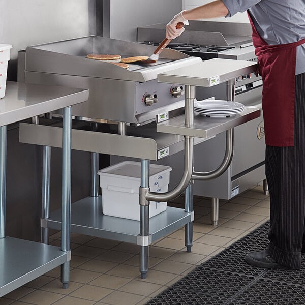 A man cooking food on a stainless steel Regency equipment stand with plates on a shelf.