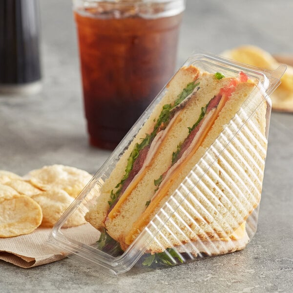A sandwich in a Choice PET sandwich wedge container next to a glass of iced tea.