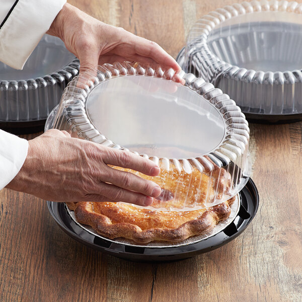 A person putting a pie into a Baker's Mark plastic container with a clear high dome lid.