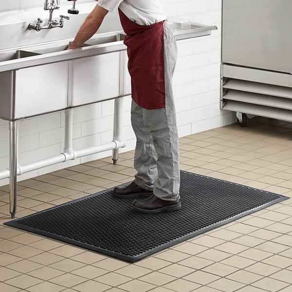 A man standing on a black Choice rubber ridge-scraper mat in a kitchen.