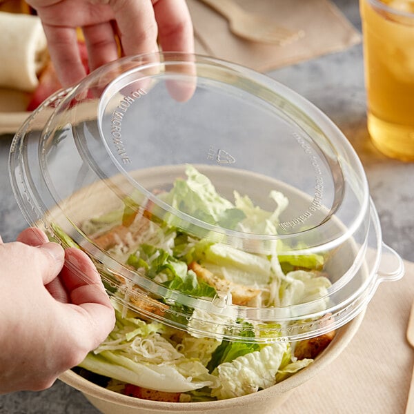 A hand holding a Tellus Products plastic dome lid over a salad.