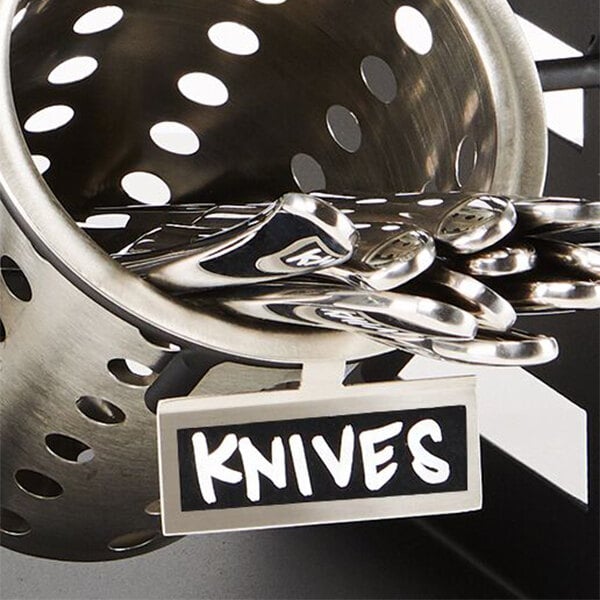 A stainless steel container with a black and white chalkboard label with white text holding knives.