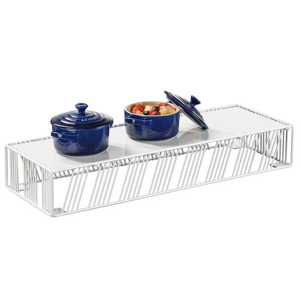 A white metal rectangular display riser holding blue pots and white bowls.